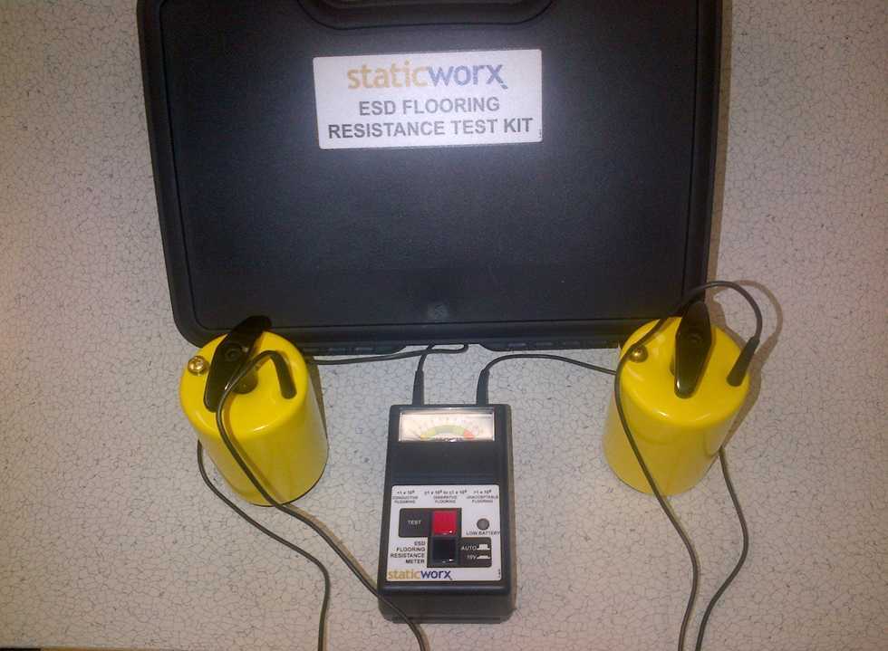 Photo of a resistance test kit. The black case is in the top half of the photo with a label that reads “ESD flooring resistance test kit” with the StaticWorx logo about. In front of the case are two probes and an analog surface resistance meter.