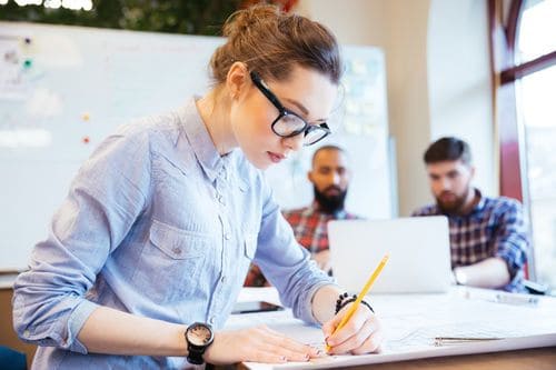 Photo of a female architect working at a desk. Two male architects can be seen in the background.